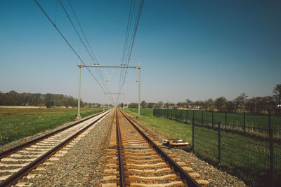 Diminishing perspective of railroad tracks against clear blue sky