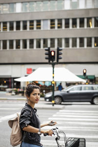 Portrait of woman with bicycle holding mobile phone while standing on city street