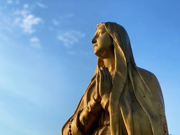 Gold statue of virgin mary at sunset against blue sky.