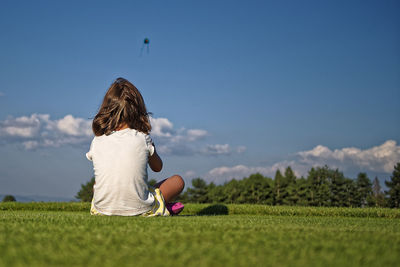 Rear view of girl sitting on field against blue sky