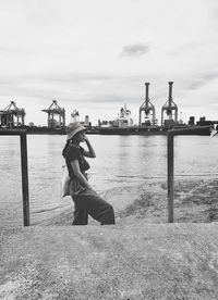 Side view of woman sitting on riverbank against sky