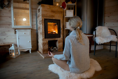 A woman meditates in a cozy home atmosphere by the fireplace