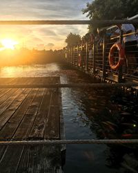 Railroad tracks by river against sky during sunset
