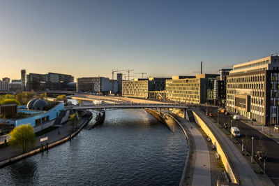 Bridge over river amidst buildings against clear sky during sunset