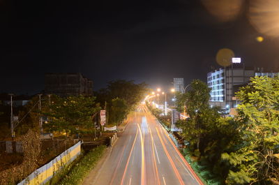 Road by illuminated buildings in city against sky at night