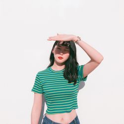 Portrait of young woman shielding eyes standing against wall