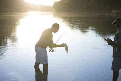 Side view of male friends fishing in lake during sunset