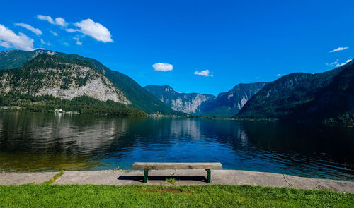 Empty bench at lakeshore by mountains against sky