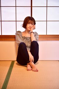 Young woman looking away while sitting on window at home