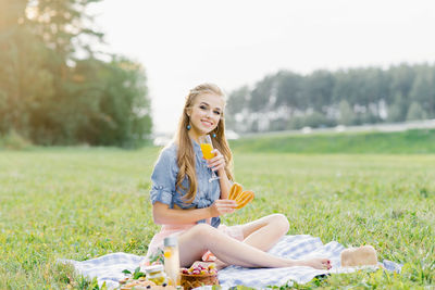 Pretty caucasian young woman with long hair is lsitting on a blanket in nature
