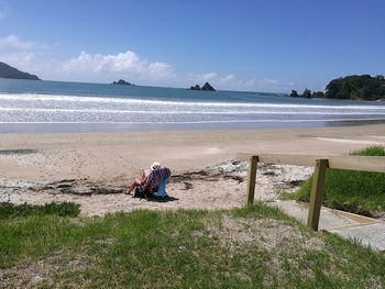 Man sitting on beach against sky