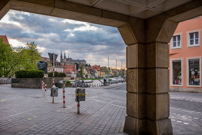 City street by buildings against cloudy sky