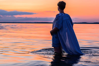 Rear view of woman standing in sea during sunset