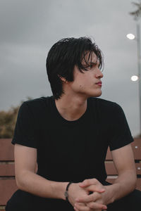 Young man looking away while sitting against sky