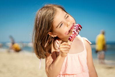 Cute girl looking away while eating ice cream at beach