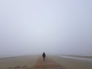 Rear view of woman standing amidst fog at beach