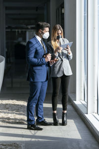 Professionals with protective face mask working over digital tablet while standing in office
