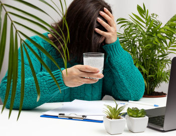 Woman in a sweater sits at the table with her head clasped in her hands, stress and 