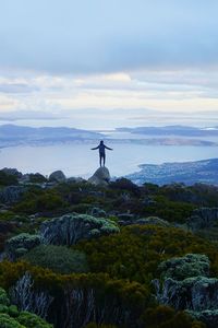 Man standing on rock by lake against sky