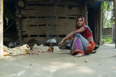 Portrait of young woman sitting outdoors making food on wood burning stove