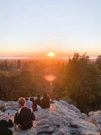 Rear view of people sitting on rock against sky during sunset