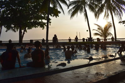 People sitting by swimming pool against sky