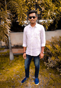 Young man wearing sunglasses standing against plants