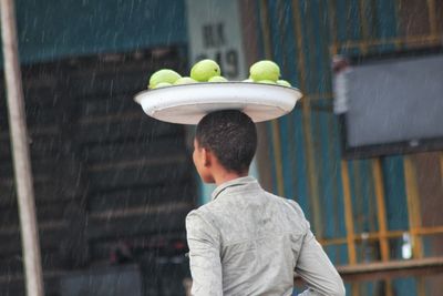 Rear view of girl carrying fruits in tray on head during rainy season