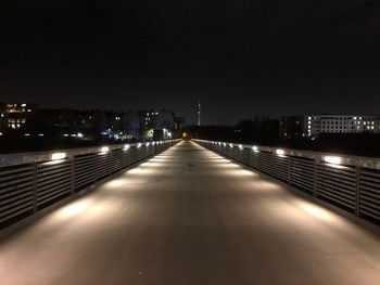 Illuminated street amidst buildings against sky at night