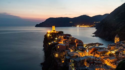 High angle view of illuminated building by sea against sky at sunset