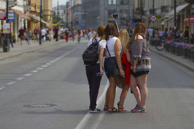 Rear view of women taking selfie through monopod on street