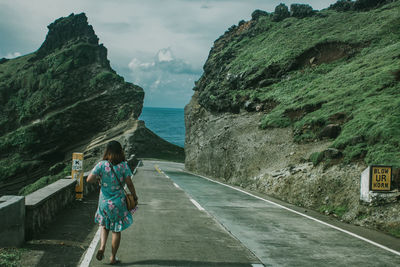 Rear view of woman on road by sea against mountain