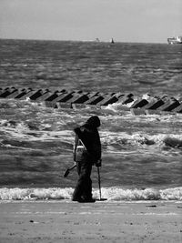 Rear view of man searching with metal detector at beach