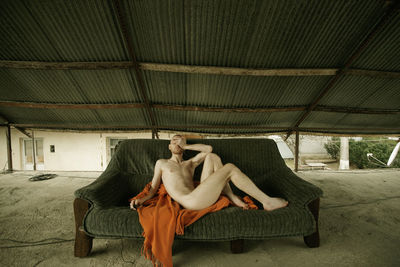Full length of naked man sitting on sofa