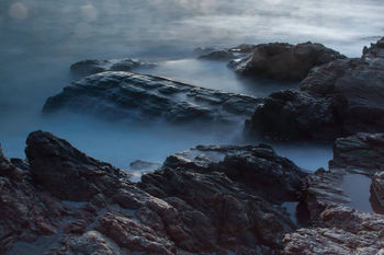 Scenic view of rock formation by sea against cloudy sky