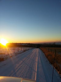 Road on snow field against clear sky during sunset