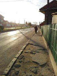 Rear view of man walking on footpath by buildings in city