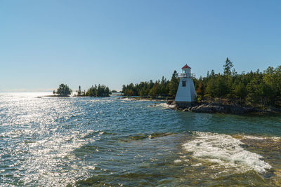 Lighthouse by sea against clear sky