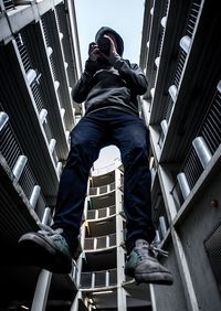 Low angle view of man in mid-air photographing through camera amidst buildings