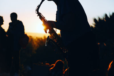 Midsection of silhouette man playing saxophone against clear sky during sunset