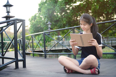 Woman reading book while sitting on field at park