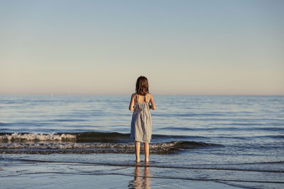 Woman standing at beach against sky during sunset