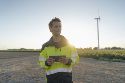 Engineer standing in rural landscape at a wind turbine holding tablet