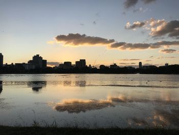 Silhouette buildings by river against sky during sunset
