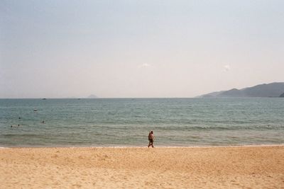 Rear view of man standing on beach against clear sky