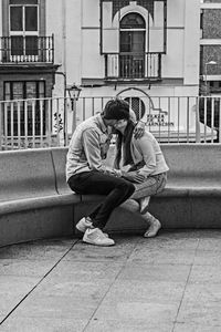 Young man sitting on sidewalk in city