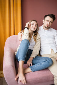 Adult brother and sister sitting smiling in a relaxed pose on couch.