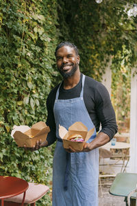 Portrait of smiling male cafe owner holding food in take away boxes