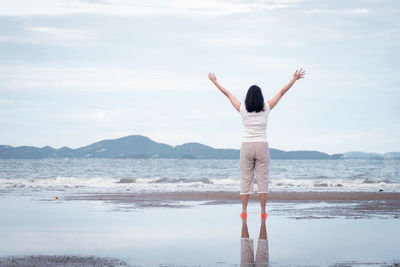 Rear view of woman standing on beach against sky