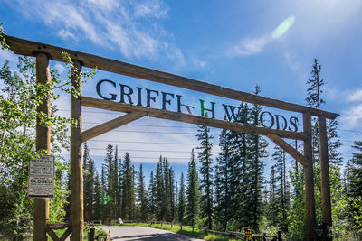 Road sign by trees against sky